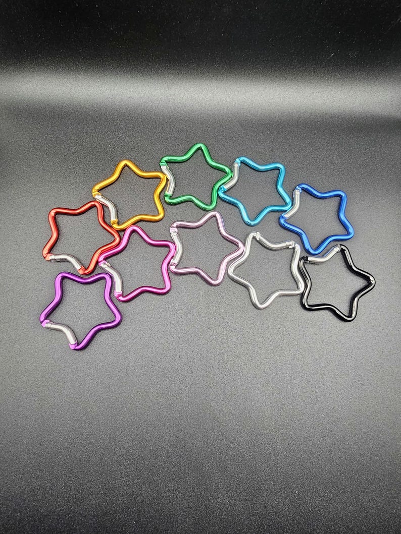 Puede incluir: Una colecci&oacute;n de diez mosquetones con forma de estrella en varios colores, incluyendo rojo, naranja, verde, azul claro, azul oscuro, rosa, morado, plateado y negro. Cada mosquet&oacute;n de metal cuenta con un mecanismo de cierre de resorte.
