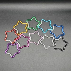 Puede incluir: Una colecci&oacute;n de diez mosquetones con forma de estrella en varios colores met&aacute;licos, incluyendo rojo, dorado, verde, azul claro, azul oscuro, morado, rosa, plateado y negro. Cada mosquet&oacute;n cuenta con un mecanismo de cierre de resorte integrado.