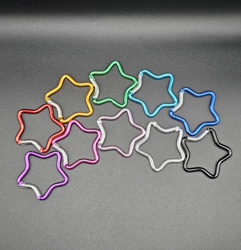 Puede incluir: Una colecci&oacute;n de diez mosquetones con forma de estrella en varios colores met&aacute;licos, incluyendo rojo, dorado, verde, azul claro, azul oscuro, morado, rosa, plateado y negro. Cada mosquet&oacute;n cuenta con un mecanismo de cierre de resorte integrado.