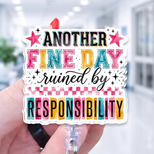 May include: A square acrylic badge reel featuring the text "ANOTHER FINE DAY ruined by RESPONSIBILITY" in colorful, multi-font lettering. The design includes pink stars, a checkered pattern, and decorative sparkles on a white background.