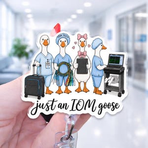 May include: An acrylic badge reel featuring four cartoon geese dressed in medical scrubs. One goose holds a suitcase, another holds medical cables, one holds a clipboard with a pink bow, and one operates a monitor. The text reads just an IOM goose.