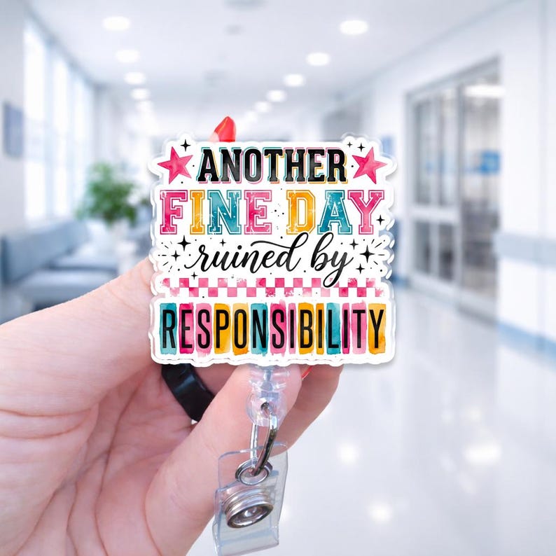 May include: A square acrylic badge reel featuring the text "ANOTHER FINE DAY ruined by RESPONSIBILITY" in colorful, multi-font lettering. The design includes pink stars, a checkered pattern, and decorative sparkles on a white background.
