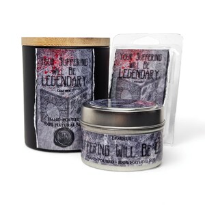 May include: Three candles in different sizes with black and silver containers. The labels on the candles say "Your Suffering Will Be Legendary" with the word "Leather" printed below. The candles are hand-poured and made with 100% natural soy.