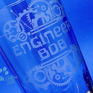 Peut inclure: Un verre bleu avec un motif gravé blanc de rouages et le texte "Engineer Bob".