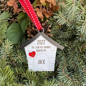 May include: A wooden dog house ornament with a red heart and the text "2022 The year my humans adopted me Jack".