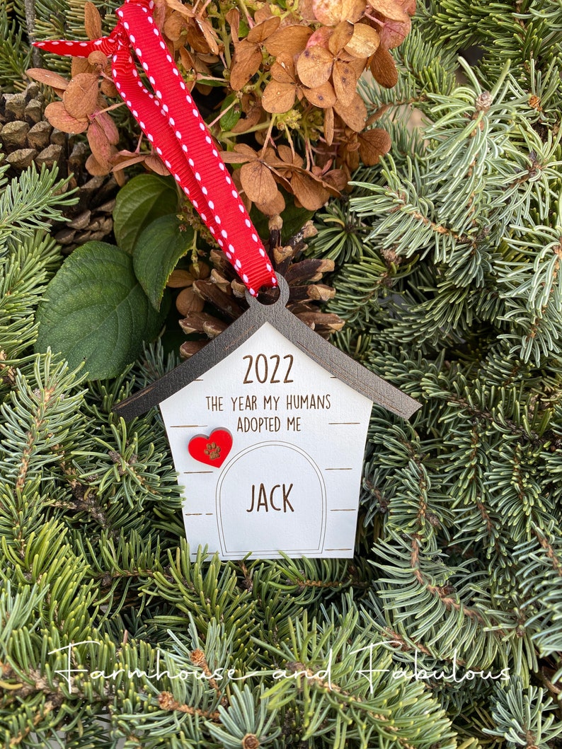 May include: A wooden dog house ornament with a red heart and the text "2022 The year my humans adopted me Jack".