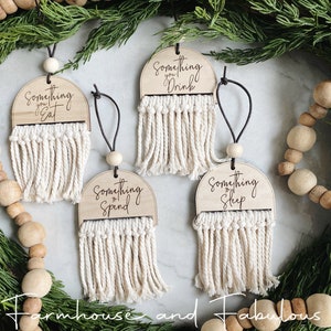 May include: Four wooden ornaments with macrame fringe and the phrases "Something you Eat", "Something you Drink", "Something to Spend", and "Something to Sleep". Each ornament has a wooden bead and a black string for hanging.