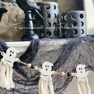 Puede incluir: Una guirnalda de fantasmas blancos con cuentas negras y de madera natural, borlas blancas y el texto "Farmhouse and Fabulous" sobre un fondo blanco y negro.