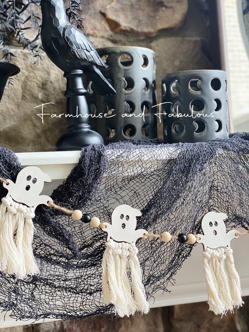 Puede incluir: Una guirnalda de fantasmas blancos con cuentas negras y de madera natural, borlas blancas y el texto "Farmhouse and Fabulous" sobre un fondo blanco y negro.