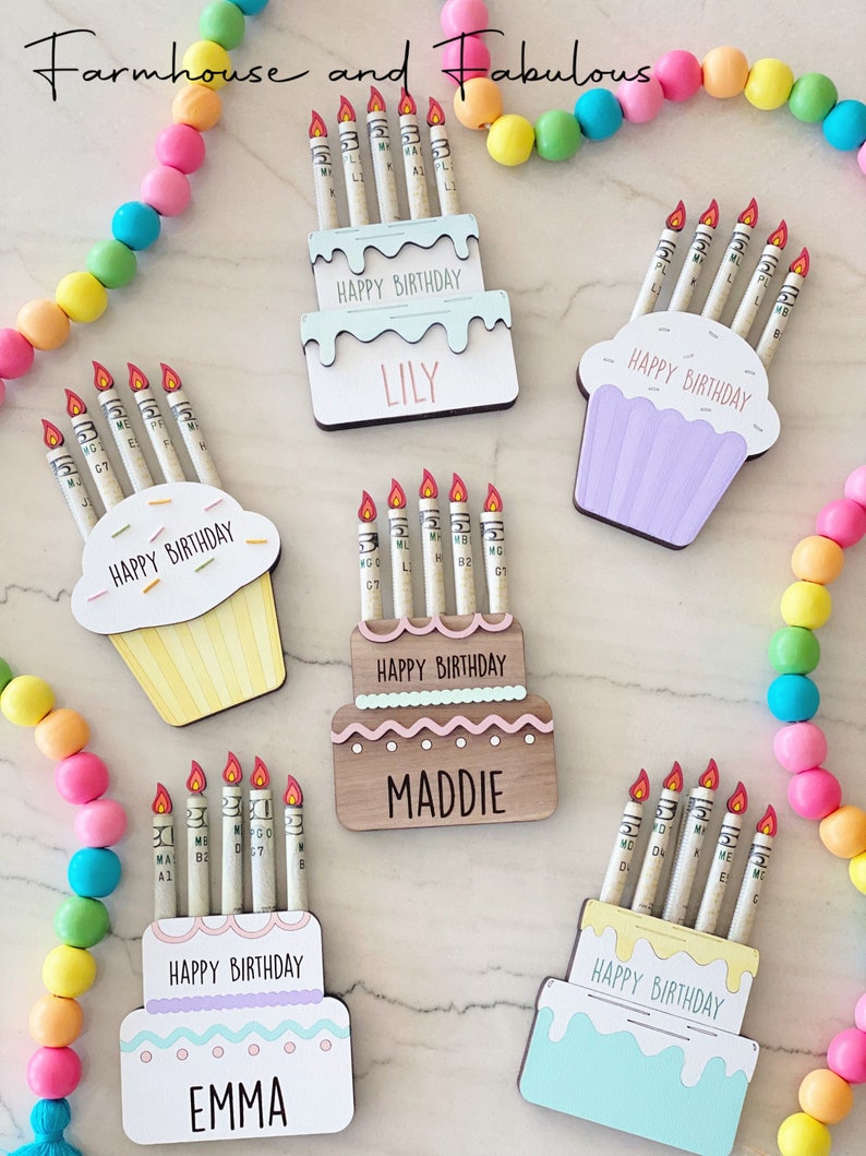 May include: Five birthday cake decorations with candles made of rolled up dollar bills. The cakes are decorated with frosting and sprinkles. The cakes are labeled with the names Lily, Maddie, and Emma. The text "Happy Birthday" is on each cake.