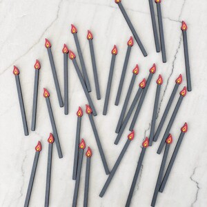 May include: A collection of 25 black wooden matchsticks with red and orange flame tips scattered on a white marble surface. The text "Farmhouse and Fabulous" is written in black cursive at the bottom of the image.