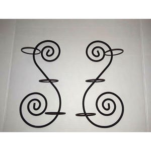 May include: Two decorative, wrought iron wall sconces. Each sconce features a swirling design with three circular holders for candles or small items. The metal has a dark brown finish, and the design is symmetrical.