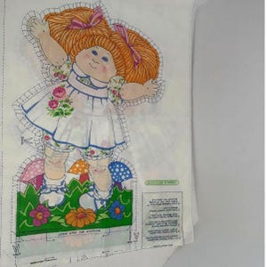 May include: A Cabbage Patch Kids fabric panel featuring a doll with orange hair, a white dress with blue trim, and floral accents. The doll is surrounded by mushrooms and flowers. The text "LEAVE OPEN FOR STUFFING" is visible.