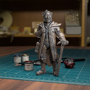 May include: A bronze painted miniature figurine of a character wearing a long coat, holding a staff and a book. The figurine is standing on a green cutting mat with paint pots and a dice.