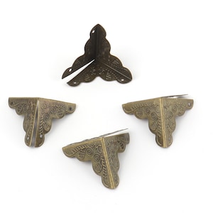 May include: Four antique gold corner protectors with ornate floral designs. The protectors are made of metal and have a distressed finish.