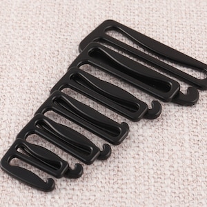 May include: A set of seven black plastic bra strap adjusters. The adjusters are in different sizes, with the largest at the top and the smallest at the bottom.