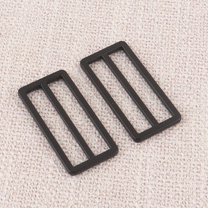Puede incluir: Dos hebillas deslizantes de metal negro con forma rectangular y dos l&iacute;neas paralelas que atraviesan el centro.