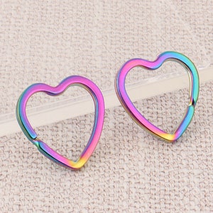 May include: Two heart-shaped metal clasps with a rainbow iridescent finish. The clasps are open, revealing a small hinge. The heart shapes are smooth and polished, reflecting a spectrum of colors.