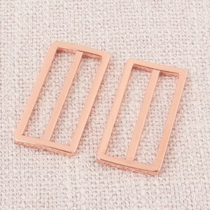 Puede incluir: Dos hebillas rectangulares de metal color oro rosa con un dise&ntilde;o de doble barra.