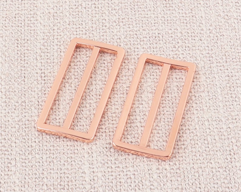 Puede incluir: Dos hebillas rectangulares de metal color oro rosa con un dise&ntilde;o de doble barra.