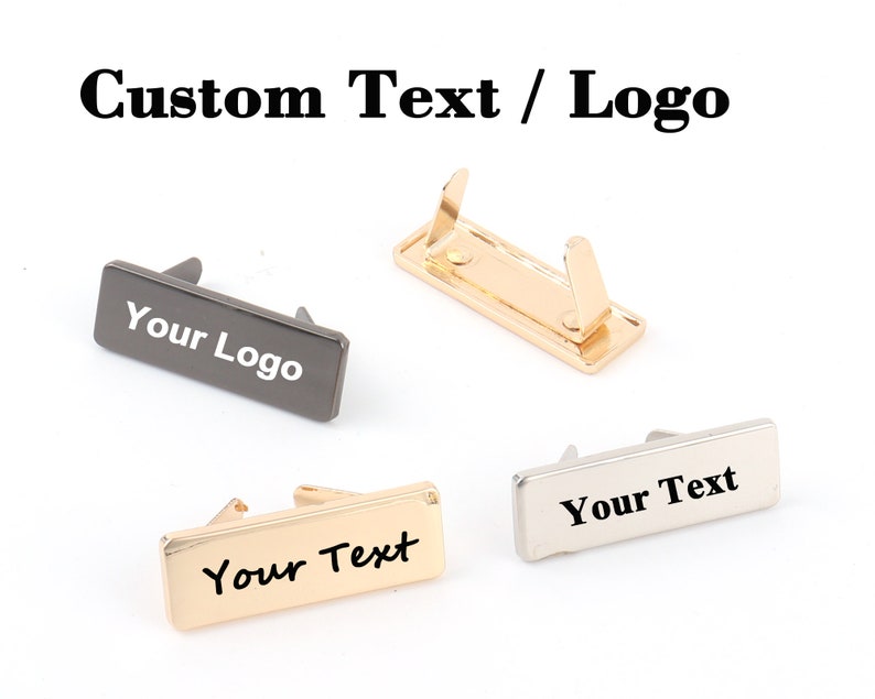 K&ouml;nnte beinhalten: Vier Metall-Namensschildhalter in Gold, Silber und Gunmetal-Grau. Jedes Schild hat eine rechteckige Form mit gew&ouml;lbter Oberseite und einem Clip auf der R&uuml;ckseite. Die Schilder zeigen den Text "Your Logo" oder "Your Text" in Wei&szlig; oder Schwarz.