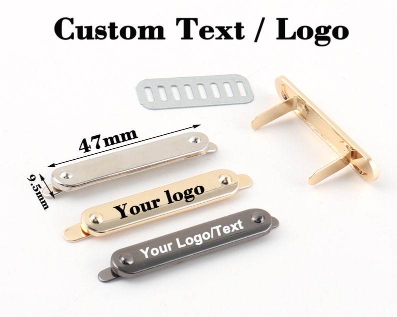 May include: Three metal rectangular tags with rounded edges. The tags are silver, gold, and black. Each tag has two small metal loops on the back. The gold tag has the text "Your logo" printed on it. The black tag has the text "Your Logo/Text" printed on it. The tags are 4.7 cm long and 0.95 cm wide.