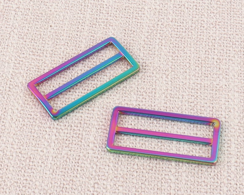 Puede incluir: Dos hebillas deslizantes de metal iridiscente. Las hebillas son rectangulares con dos barras paralelas en el interior. Las hebillas son un arco&iacute;ris de colores, incluyendo rosa, azul, verde y morado.