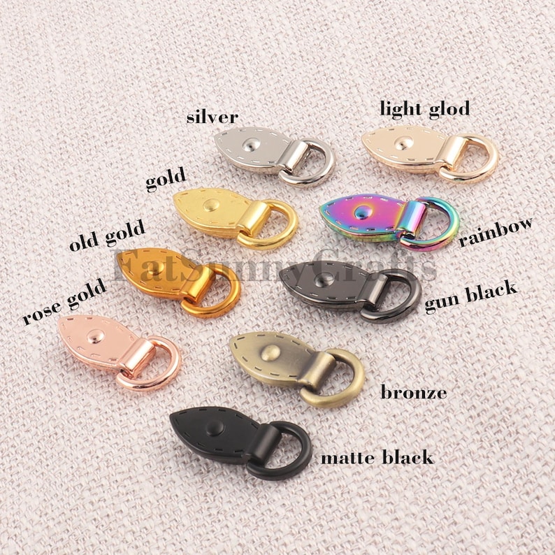 May include: A collection of decorative toggle clasps in various metallic finishes, including silver, gold, rose gold, and gun black. Each clasp features a rounded, stitched design with a loop for attachment. The image also includes a rainbow and bronze clasp.