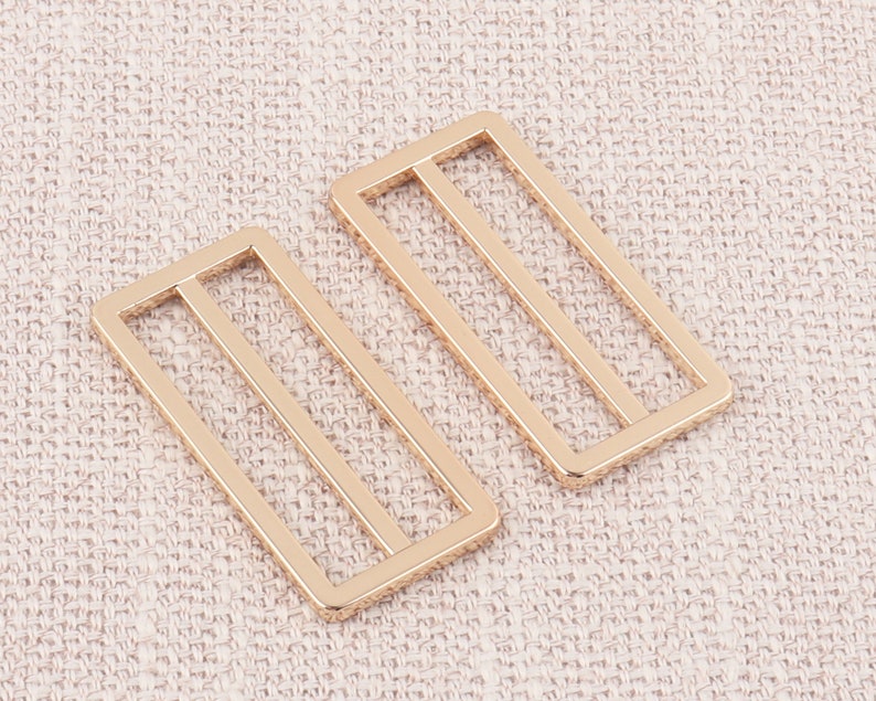 Puede incluir: Dos hebillas deslizantes de metal dorado con forma rectangular y tres l&iacute;neas paralelas.