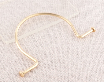May include: A gold-toned metal bangle bracelet with a unique, curved design. The bracelet has a simple, minimalist style and is secured with a screw closure.