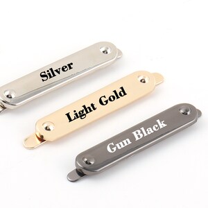 May include: Three metal rectangular clasps in silver, light gold, and gun black finishes. Each clasp has a rounded end and a small raised dot on the top. The clasps are labeled "Silver", "Light Gold", and "Gun Black".