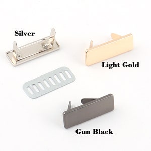 K&ouml;nnte beinhalten: Drei Metall-Handtaschenverschl&uuml;sse in Silber, Hellgold und Gun Black. Jeder Verschluss ist rechteckig mit zwei Stiften zur Befestigung. Ein silbernes Metallteil mit mehreren L&ouml;chern ist ebenfalls enthalten. Der Text "Silver", "Light Gold" und "Gun Black" wird angezeigt.