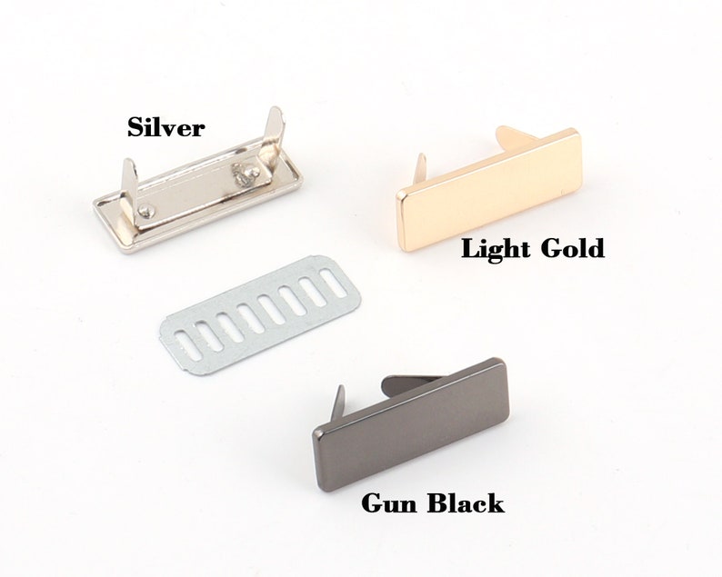 K&ouml;nnte beinhalten: Drei Metall-Handtaschenverschl&uuml;sse in Silber, Hellgold und Gun Black. Jeder Verschluss ist rechteckig mit zwei Stiften zur Befestigung. Ein silbernes Metallteil mit mehreren L&ouml;chern ist ebenfalls enthalten. Der Text "Silver", "Light Gold" und "Gun Black" wird angezeigt.
