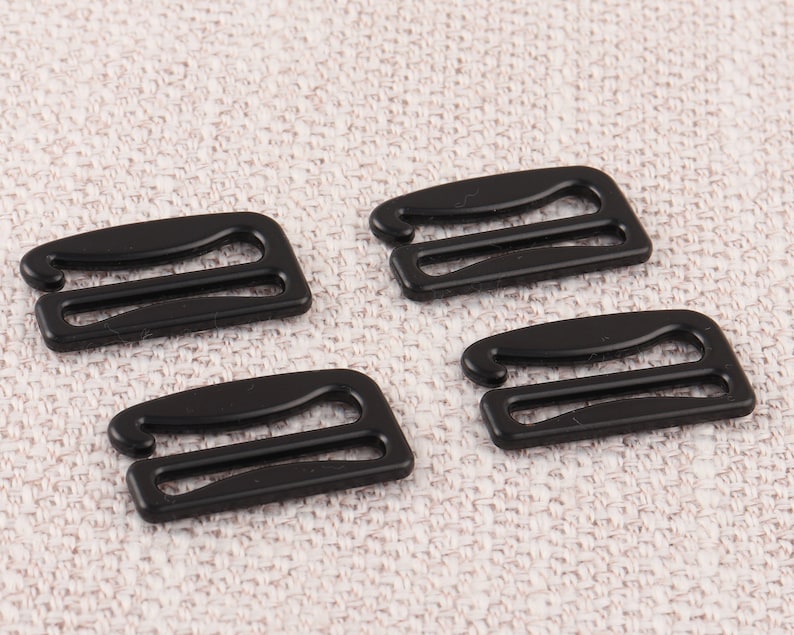May include: Four black plastic bra strap adjusters. The adjusters have two loops and are designed to be used with bra straps.