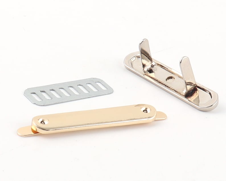 May include: A set of three metal hardware pieces for attaching a strap or handle to a bag or other project. The pieces are silver, gold, and a silver plate with holes.