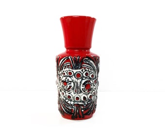 Puede incluir: Un jarrón de cerámica rojo con un diseño geométrico en blanco y negro. El jarrón tiene una boca ancha y una base estrecha.