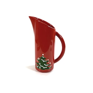May include: Red ceramic jug with a green Christmas tree design. The tree has white lights and a star on top.