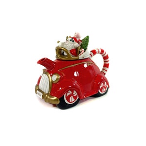 May include: Red ceramic teapot shaped like a vintage car with a candy cane spout and Santa Claus riding in the back with a Christmas tree and candy canes.