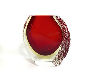 May include: A red glass vase with a textured, clear glass exterior. The vase has a rounded, oval shape.