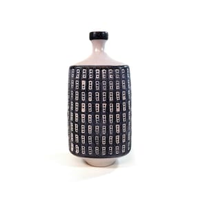 Puede incluir: Un jarrón de cerámica con cuerpo cilíndrico y cuello estrecho. El jarrón presenta un patrón azul oscuro de formas rectangulares sobre un fondo blanco. La parte superior e inferior son blancas y el cuello es negro.