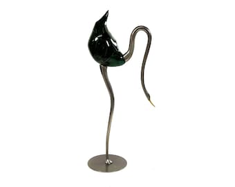 Op de afbeelding: Decoratieve metalen sculptuur van een vogel met een donkergroen, druppelvormig lichaam en een lange, gebogen nek. De vogel staat op een ronde basis met slanke poten. De snavel is goudkleurig.