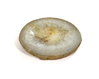 Op de afbeelding: Een dwarsdoorsnede van een geode, met een cirkelvormige vorm met een lichtbruine buitenrand en een wit en geel kristallijn interieur. De geode staat tegen een witte achtergrond, wat de natuurlijke schoonheid benadrukt.