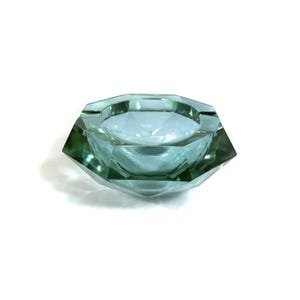 Könnte beinhalten: Ein hellgrüner Aschenbecher aus Glas mit geometrischem, facettiertem Design. Der Aschenbecher ist diamantförmig und hat eine flache Schale.