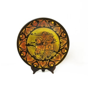 Peut inclure: Une assiette en céramique décorative avec un fond noir et un motif doré. Le motif représente un chevalier à cheval, entouré d'une bordure de cœurs.