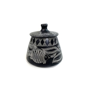 Può includere: Vaso in ceramica nera con coperchio, decorato con pesci bianchi e motivi geometrici.