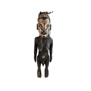 May include: A black wooden statue of a person with a carved face and a headdress. The statue is decorated with white and brown paint and has a beaded necklace.