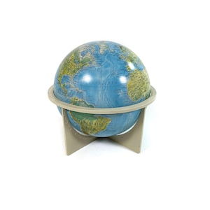 Peut inclure: Un petit globe terrestre bleu avec un socle beige. Le globe montre les continents et les océans du monde. Le globe est sur un fond blanc.