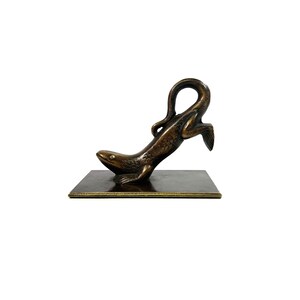 May include: Bronze sculpture of a lizard in a dynamic pose, mounted on a rectangular base. The lizard's body is detailed with scales, and its tail curves upwards. The sculpture has a dark, aged finish.