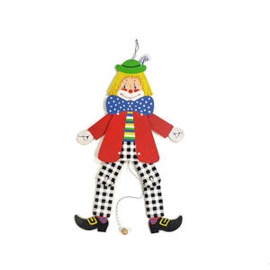 Könnte beinhalten: Holzclown-Figur mit rotem Mantel, karierter Hose und schwarzen Schuhen. Der Clown hat gelbes Haar, einen grünen Hut und einen blauen Kragen mit weißen Punkten. Eine Schnur hängt von den Beinen des Clowns.