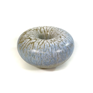 May include: A ceramic donut-shaped vase with a blue and brown glaze. The glaze has a speckled and streaky pattern.